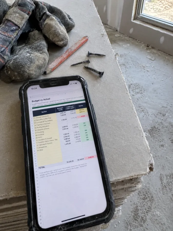 Budget versus actual job costs displayed on a phone beside drywall tools